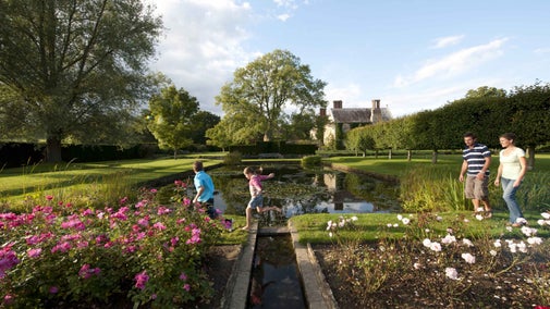 A family strolling across the top of the rectangular pond at Bateman's with the rose garden in the foreground